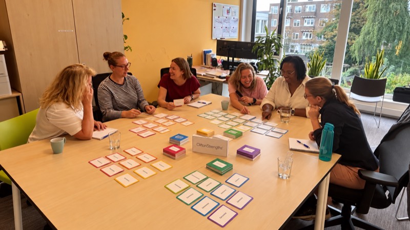 Teamsessie: zes collega's rond een tafel met CliftonStrengths®-talentkaarten